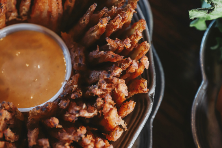 A blooming onion with dipping sauce in a metal dish.