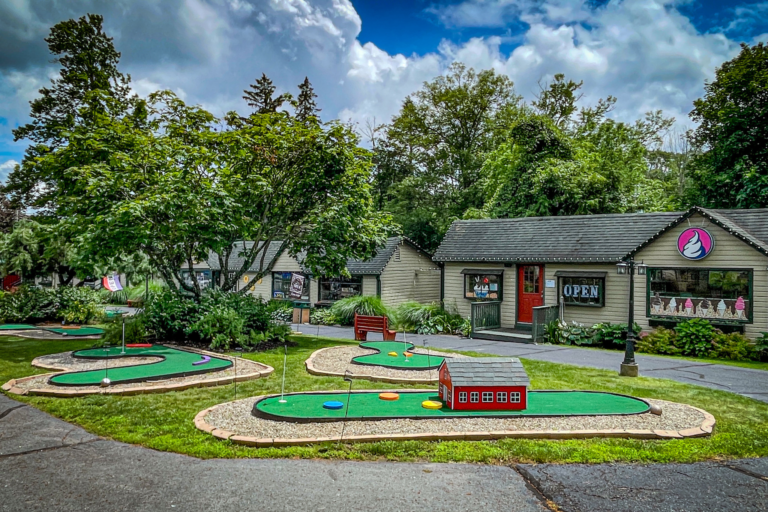 A mini golf course with a red and green theme, featuring a building in the background.