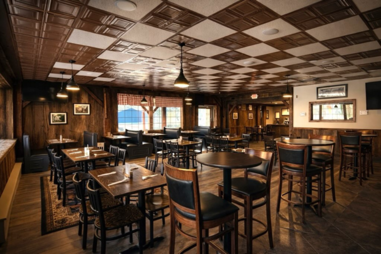 A restaurant dining area with a checkered ceiling, wooden tables and chairs, and a window in the background.